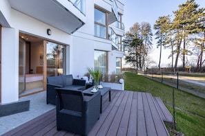 A modern outdoor seating area with a sofa and table, a glass door entrance, and a view of a grassy area with trees. - Let's Sea Gąski by 2HomeRent (Gąski)