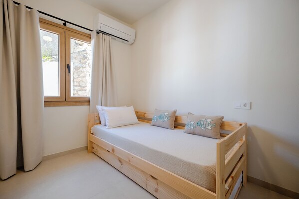 A small, single-bed room with a wooden frame, a window with curtains, and an air conditioning unit.