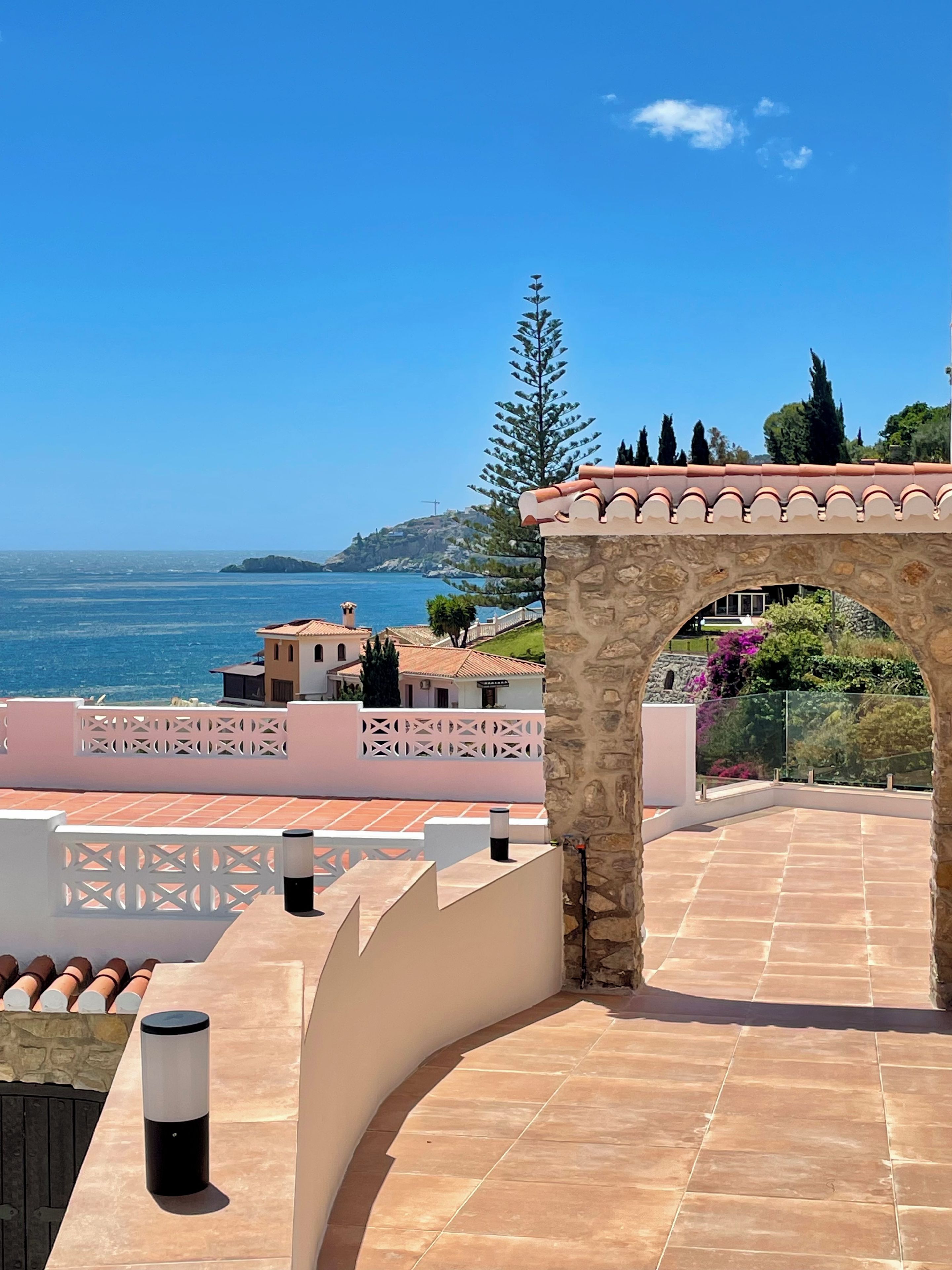 Terraço com arco de pedra, com vista para a paisagem costeira com edifícios e árvores.