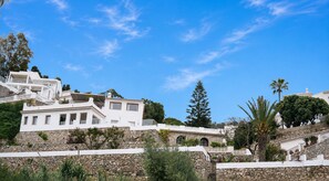 A white building with multiple levels, stone walls, and a clear blue sky.