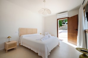 A bedroom with a bed, bedside table, lamp, and an air conditioning unit.