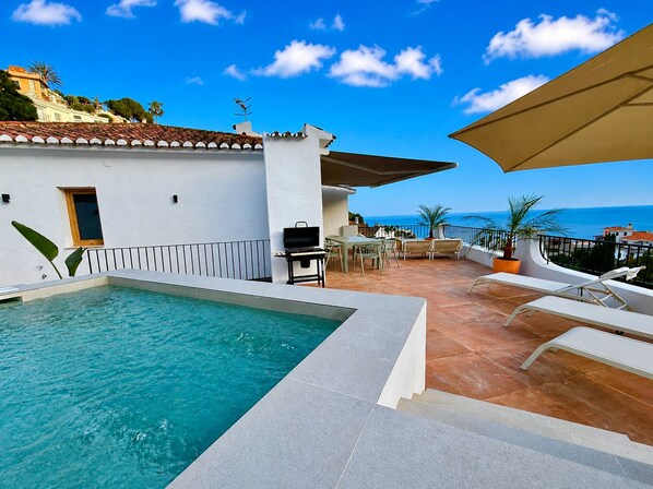 Un espace aménagé au bord de la piscine, avec vue sur la mer, comprenant du mobilier d’extérieur et un barbecue.