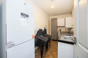 Een kleine keuken met een waterdispenser, een spoelbak en een koelkast. Er staan stoelen en een kast in de ruimte.