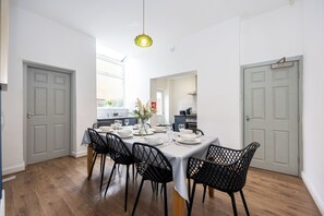 Comedor con una mesa dispuesta para cuatro personas, rodeada de sillas negras, en una habitación con paredes blancas y suelo de madera.
