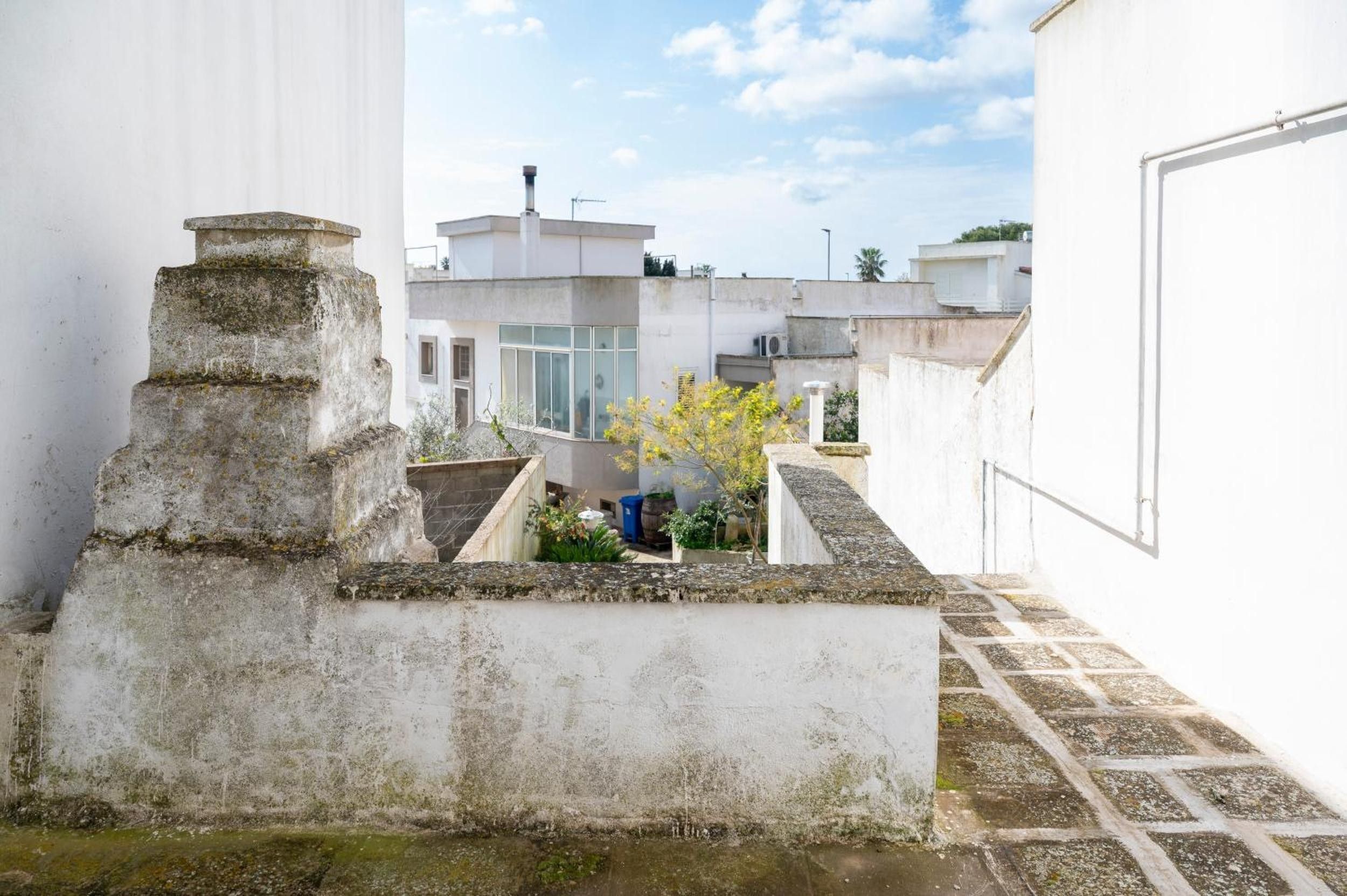 A rooftop terrace with a stone structure, a small garden area, and a view of adjacent buildings.
