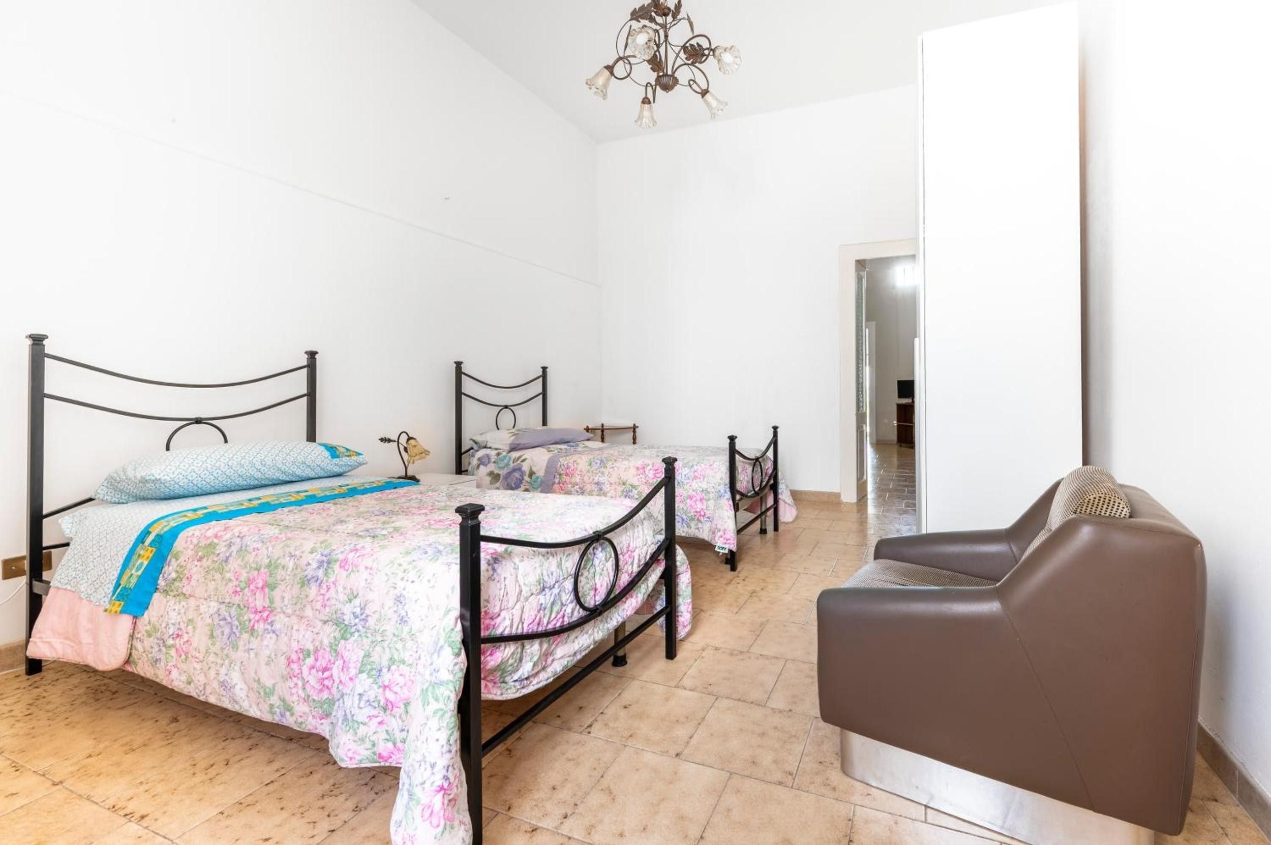 Een slaapkamer met twee enkele bedden, een bruine leren fauteuil en een kroonluchter.