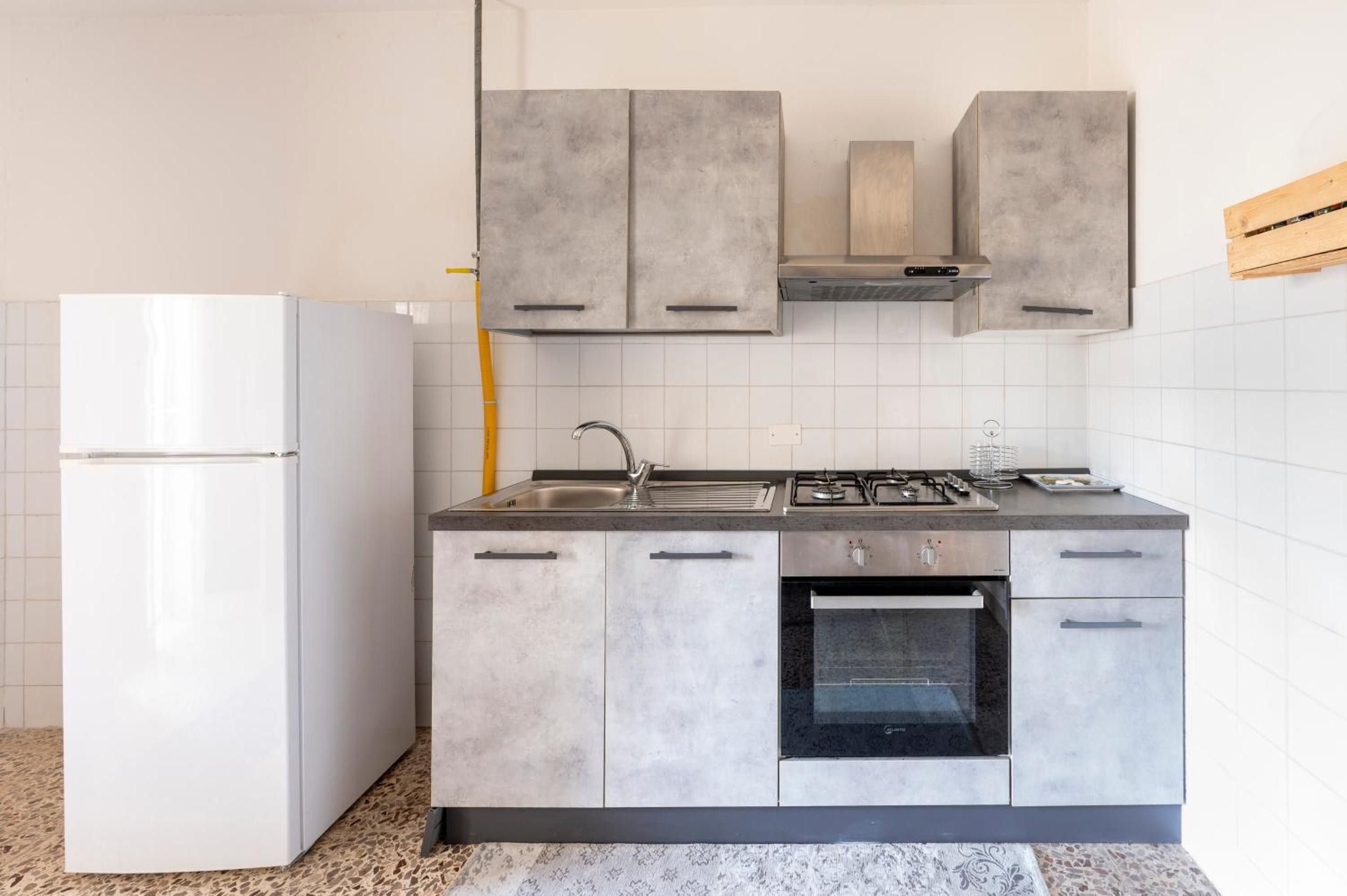 A modern kitchen with grey cabinets, a white refrigerator, a stainless steel sink, and a gas stove.