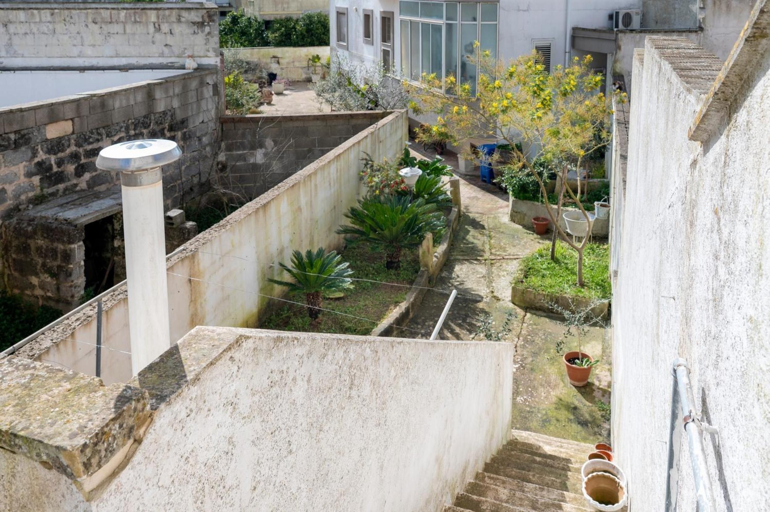 A narrow courtyard with a small garden, a water feature, and a staircase leading to an upper level.