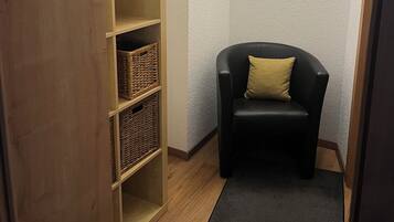 Ein Eckzimmer mit einem schwarzen Ledersessel, einem Holzbodenregal mit Körben und einer strukturierten Wand.
