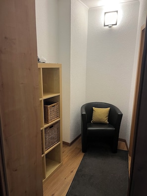 Ein Eckzimmer mit einem schwarzen Ledersessel, einem Holzbodenregal mit Körben und einer strukturierten Wand.