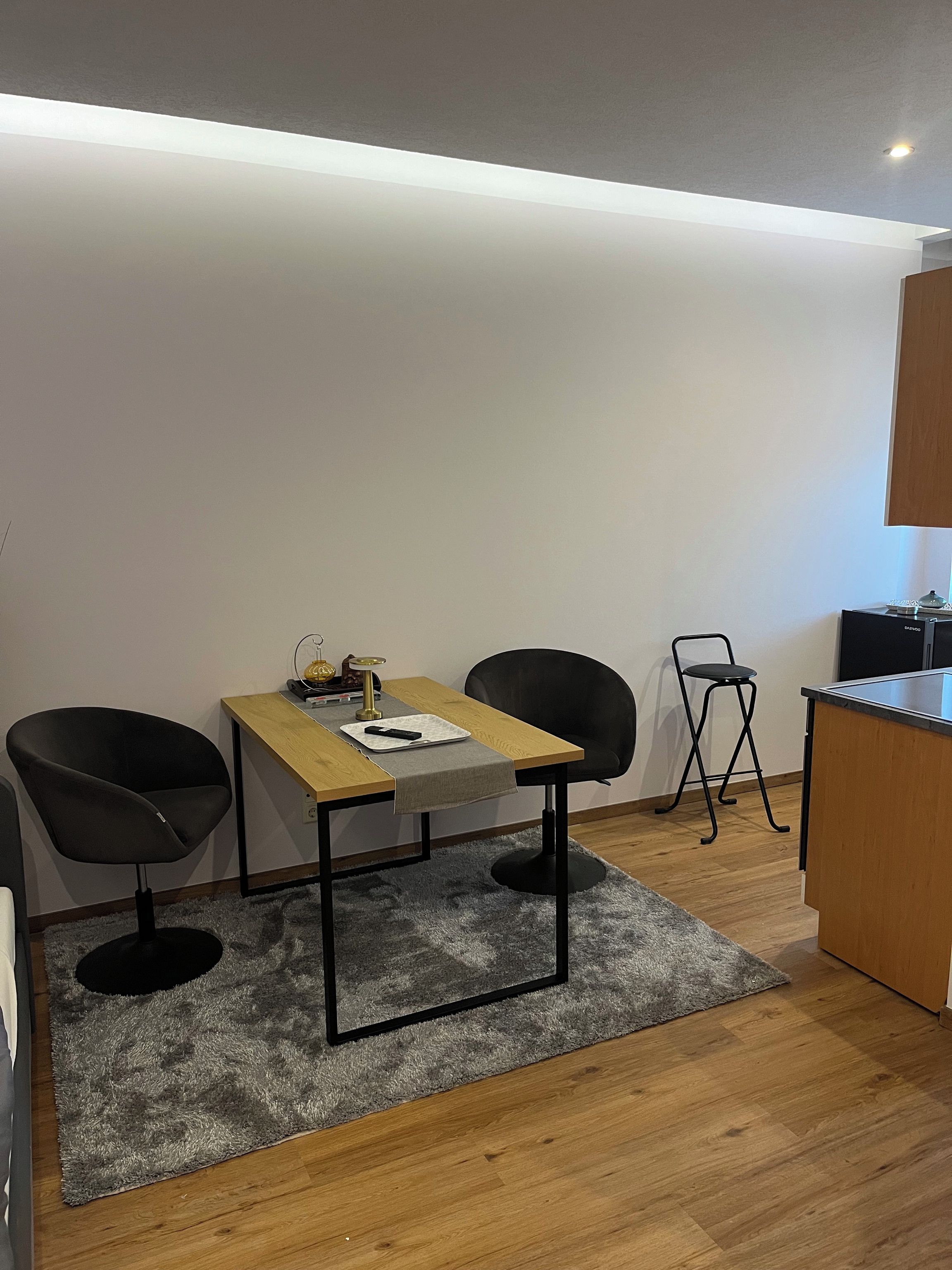 Eine moderne Küche mit einer Holz Arbeitsplatte, zwei schwarzen Stühlen, einem kleinen Tisch und einem grauen Teppich.