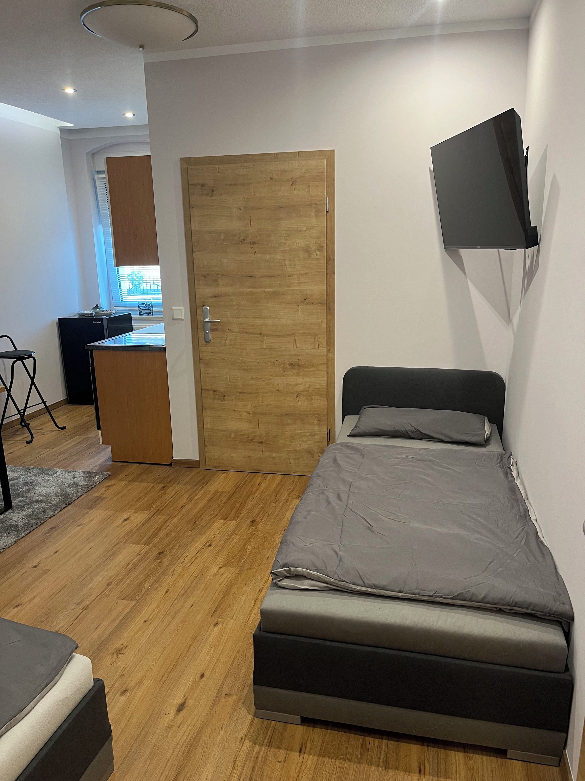 Ein Schlafzimmer mit einem Bett, einem Schreibtisch, einem Sessel und einem an der Wand befestigten Fernseher.