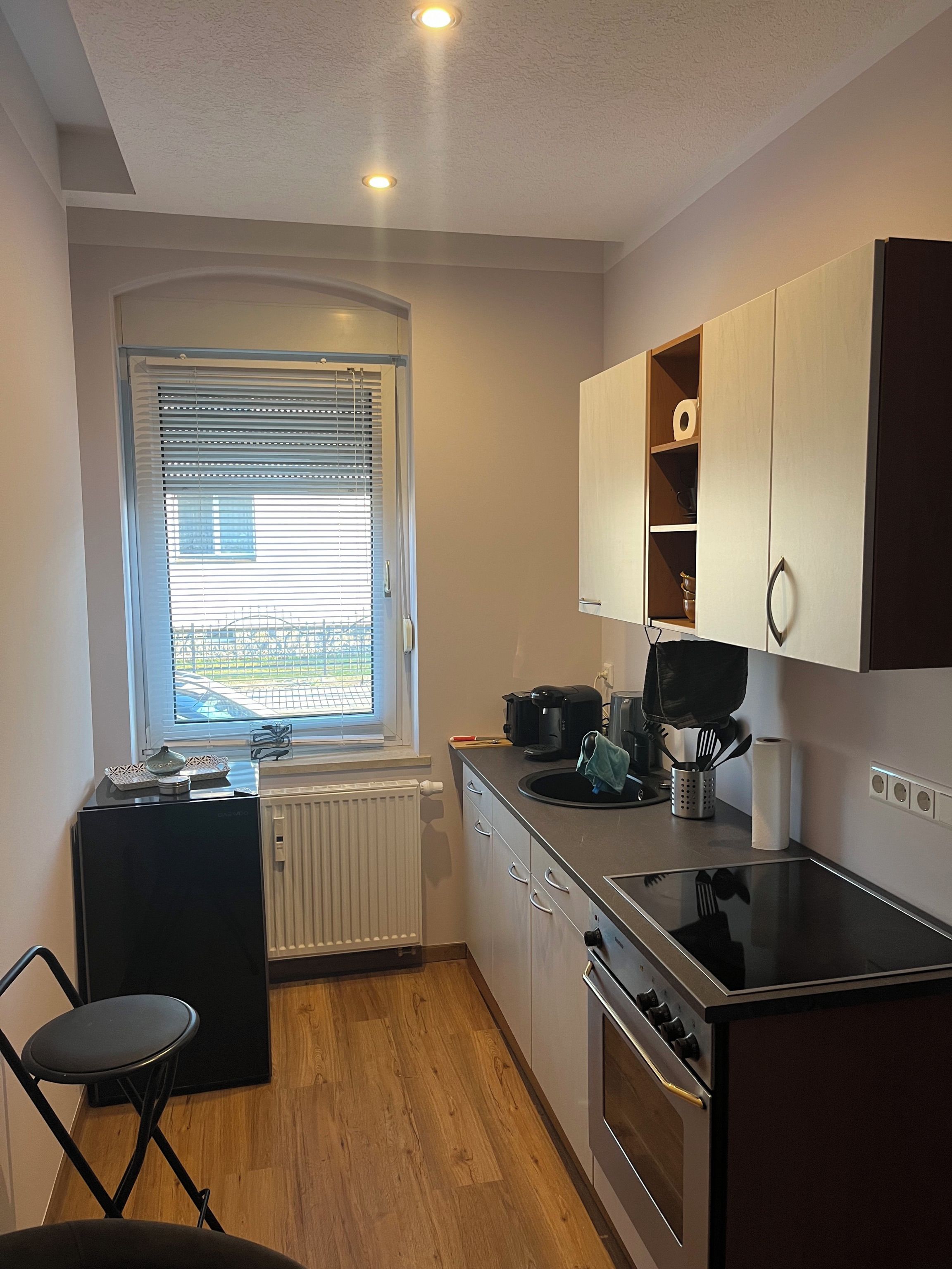 Eine kompakte Küche mit Backofen, Kaffeemaschine und einem Fenster mit Jalousien.