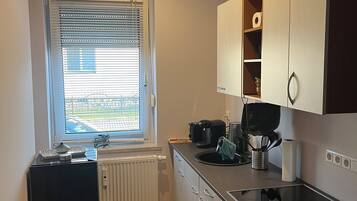 Eine kompakte Küche mit Backofen, Kaffeemaschine und einem Fenster mit Jalousien.