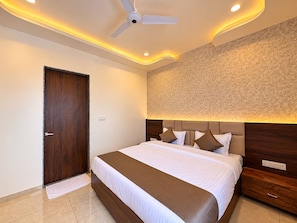 A hotel room with a bed, a ceiling fan, a textured wall, and a wooden door. - Pichola breeze a boutique stay (Udaipur)