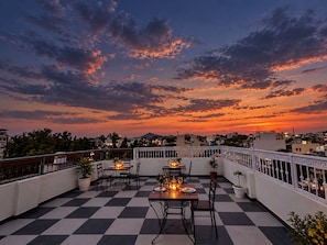 A rooftop terrace with checkered flooring, tables set for dining, and potted plants. - Pichola breeze a boutique stay (Udaipur)