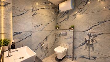 Un bany modern amb paret de marbre, un lavabo integrat, un vàter i una dutxa amb un calefactor de paret.