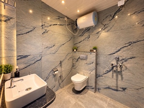 A modern bathroom with a marble wall, a built-in sink, a toilet, and a shower with a wall-mounted heater. - Pichola breeze a boutique stay (Udaipur)