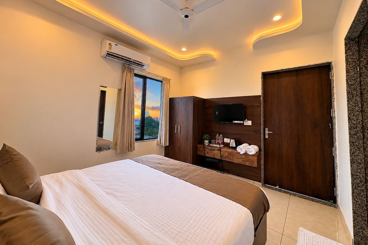 A hotel room with a bed, a television, a wardrobe, and a window with curtains.
