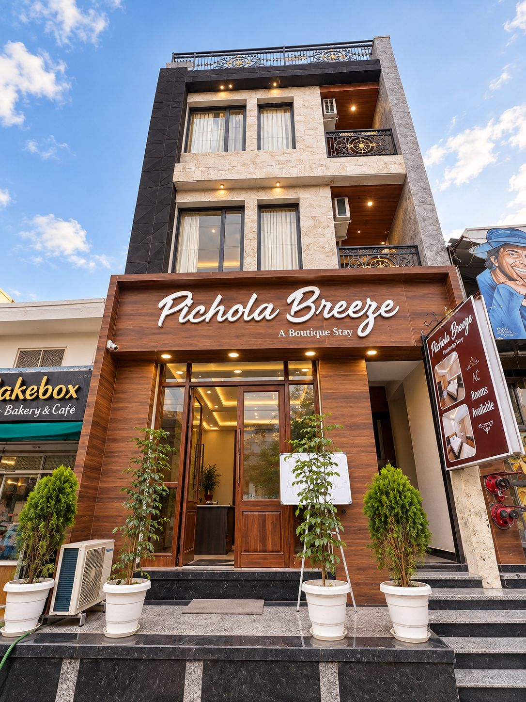 A boutique hotel named 'Pichola Breeze' with a modern facade, large windows, and a signboard advertising available rooms.