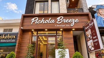 A boutique hotel named 'Pichola Breeze' with a modern facade, large windows, and a signboard advertising available rooms.