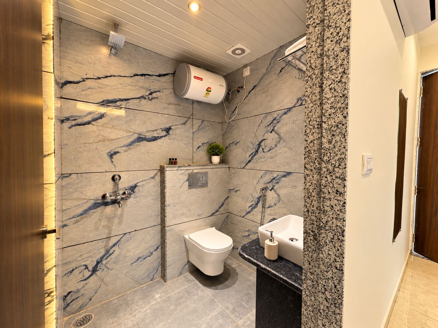 A modern bathroom with a marble wall, a toilet, a sink, and a shower.