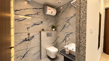 A modern bathroom with a marble wall, a toilet, a sink, and a shower.