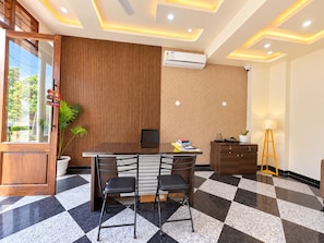 A modern office space with a checkered floor, a wooden panel wall, an air conditioning unit, a desk with chairs, and a lamp. - Pichola breeze a boutique stay (Udaipur)