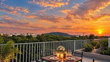 A sunset view from a balcony with a table set for two, overlooking a cityscape and greenery.