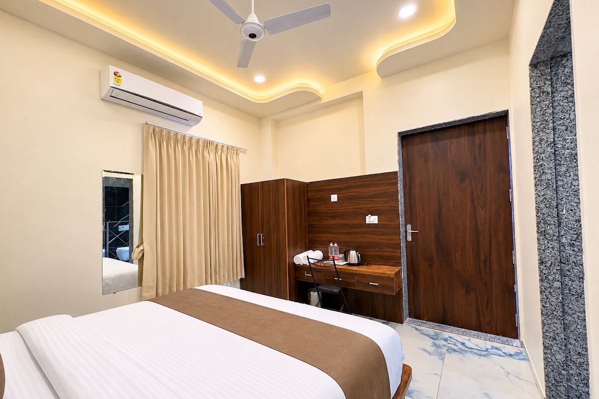 A hotel room with a bed, a desk, a wardrobe, an air conditioning unit, and a mirror.