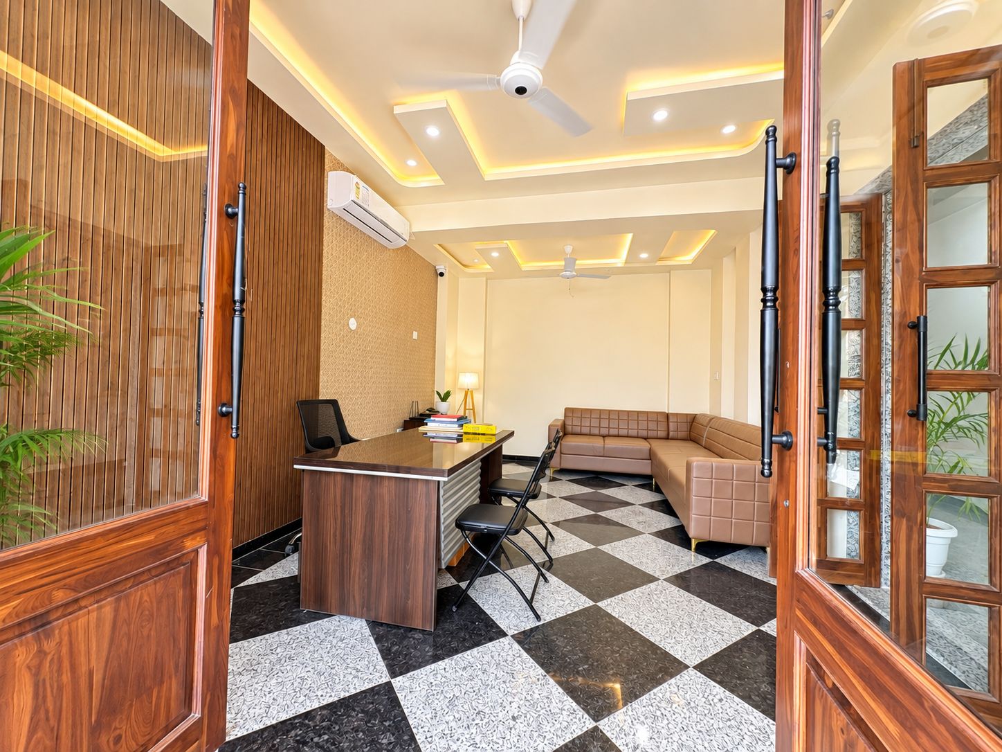 A hotel lobby with a checkered floor, a reception desk, a seating area, and a ceiling fan.