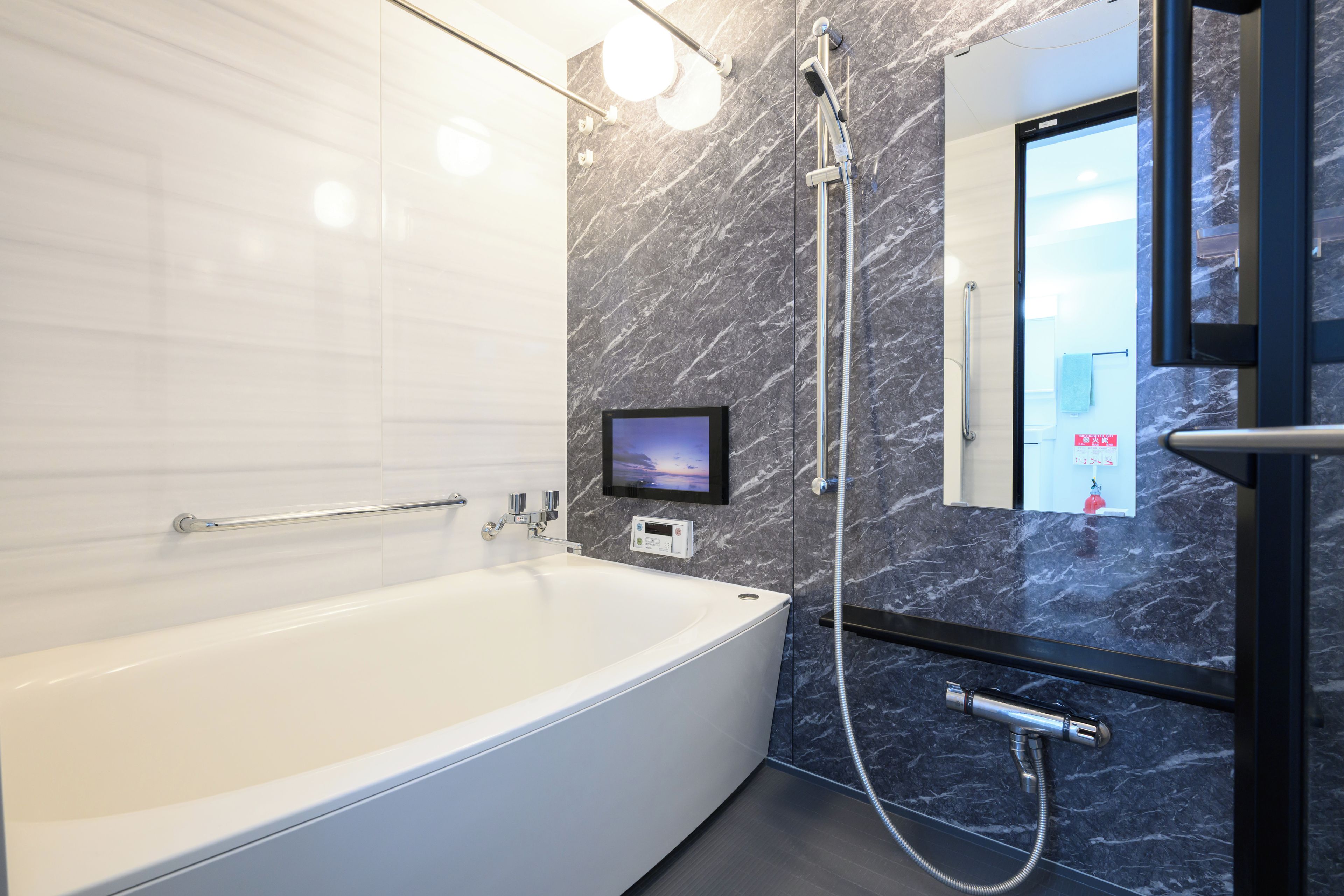 A modern bathroom with a white bathtub, a handheld showerhead, and a wall-mounted TV.