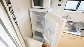 Una cocina compacta con microondas integrado, refrigerador con varios compartimentos y un lavamanos con grifo.