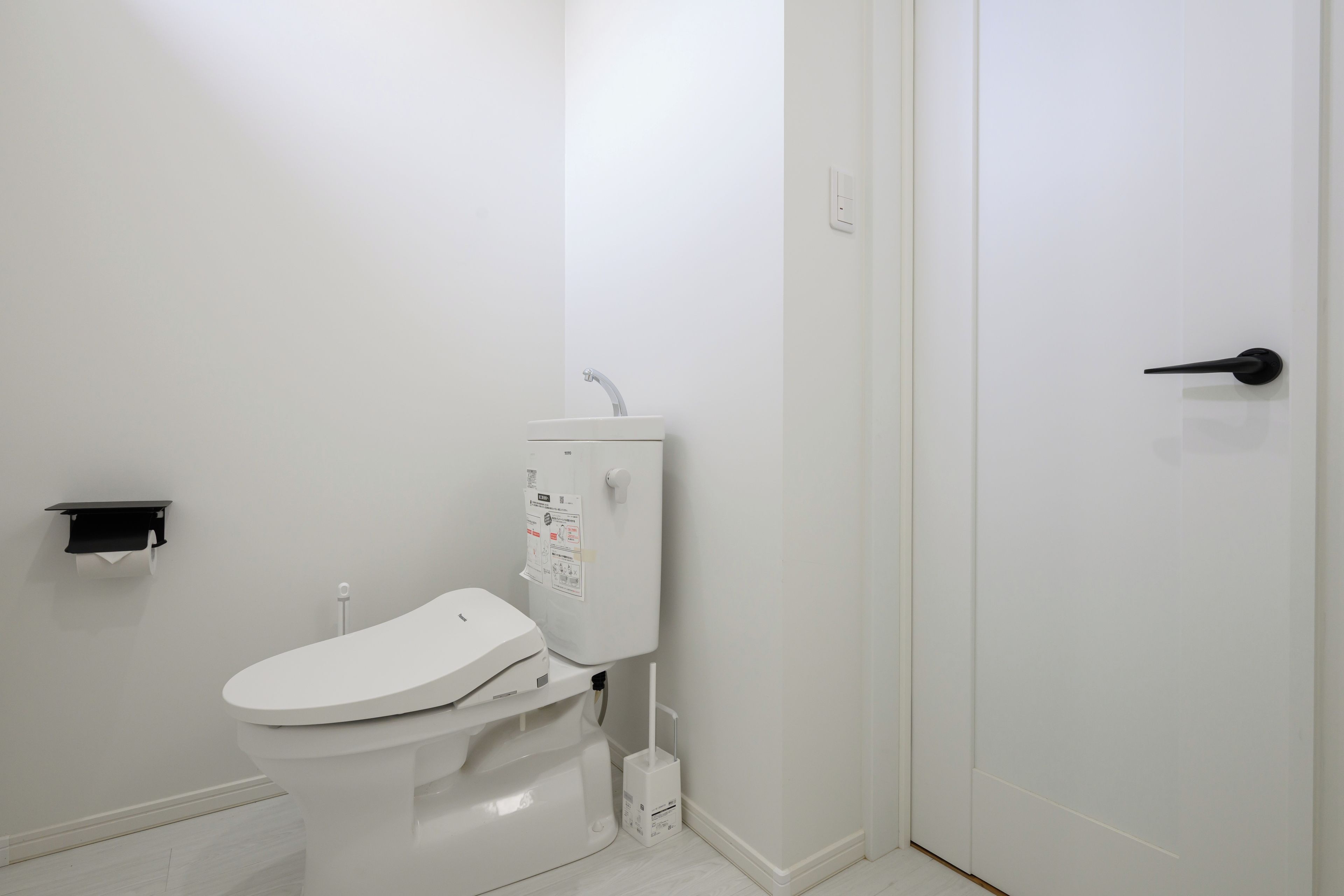 Un inodoro blanco con un dispensador de toallas de papel montado en la pared y un rollo de papel higiénico.