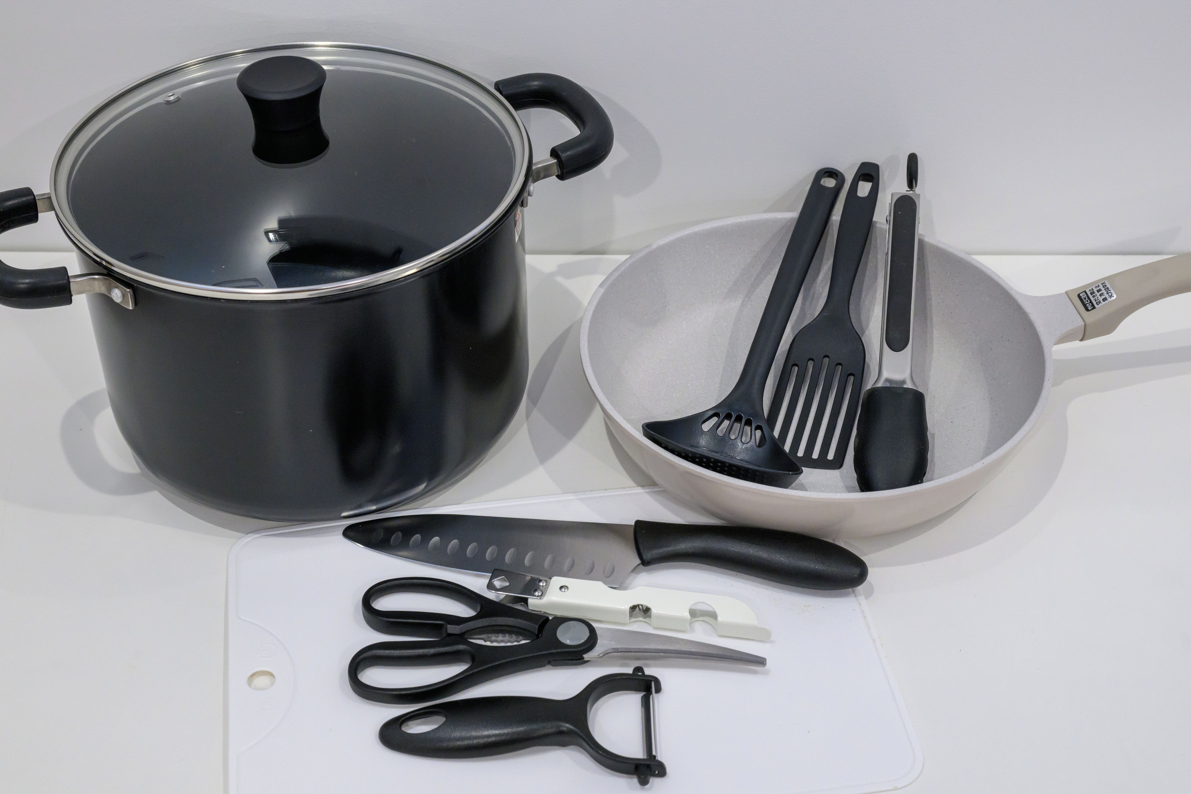A kitchen setup with a pot, a bowl of utensils, a cutting board, and a pair of scissors.