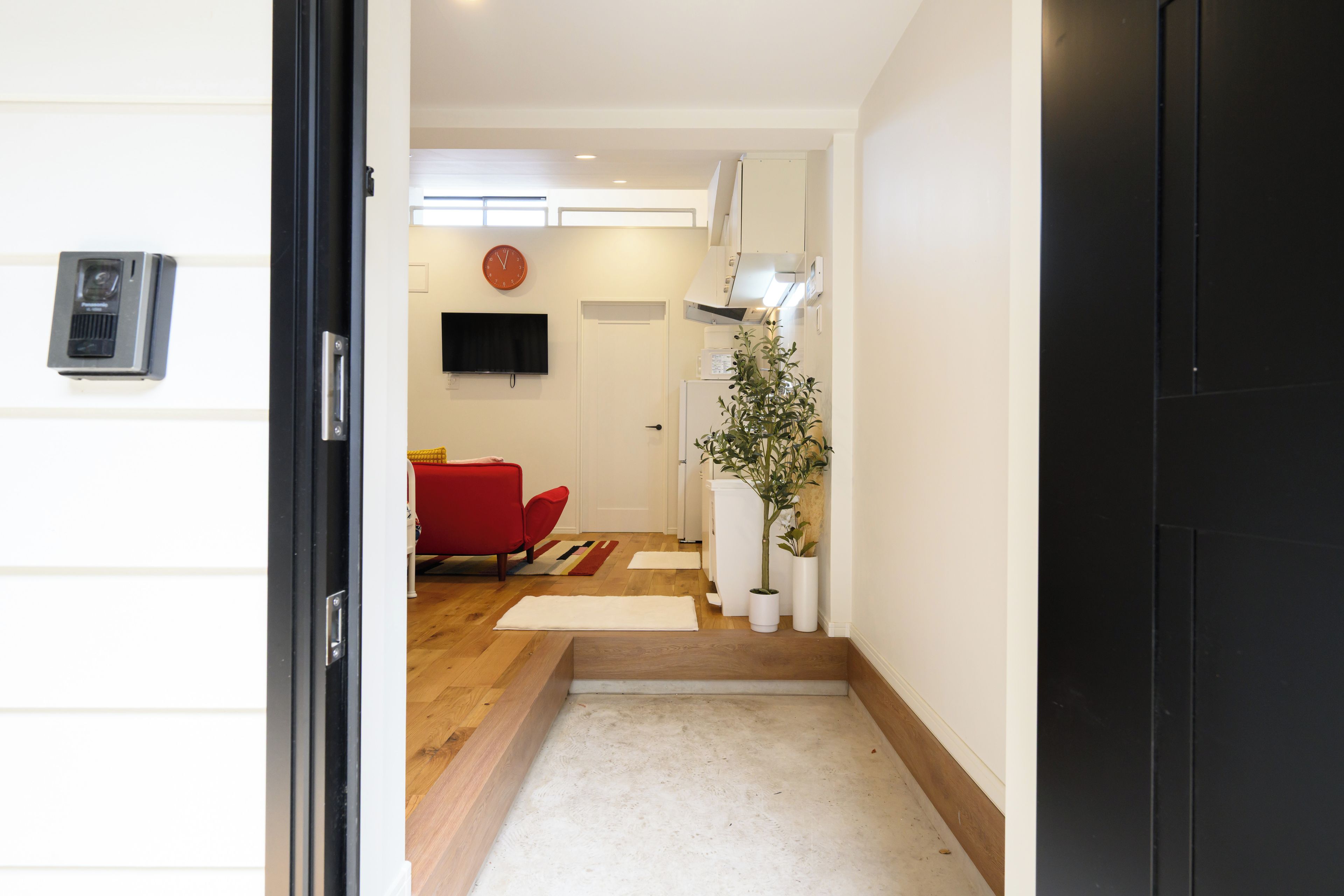 A hallway leading to a living area with a red sofa, a flat-screen TV, and a clock on the wall.