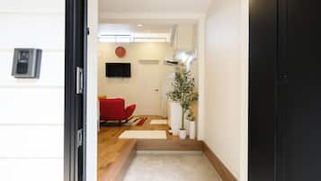 A hallway leading to a living area with a red sofa, a flat-screen TV, and a clock on the wall.