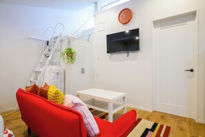 A modern living room with a red sofa, a white table, a TV mounted on the wall, a white door, and a staircase with a plant. - Villa Shimabara (Kyoto)
