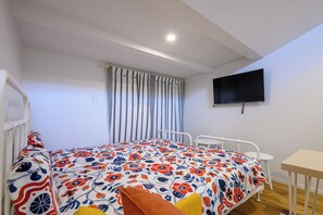 A bedroom with a bed, a bedside table, a TV mounted on the wall, and a window with curtains. - Villa Shimabara (Kyoto)