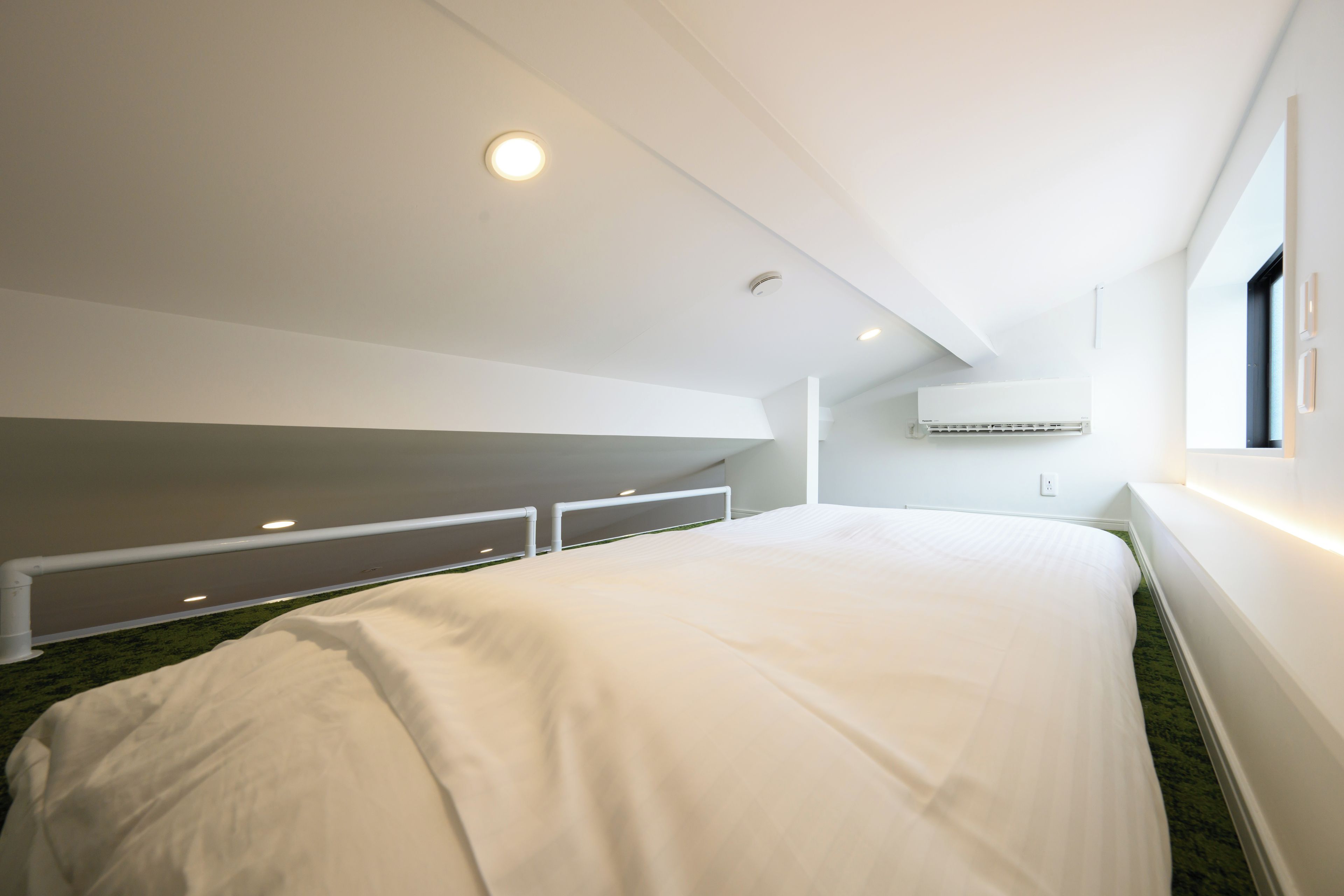 A modern bedroom with a large bed, built-in storage, a ceiling light, and a wall-mounted air conditioning unit.