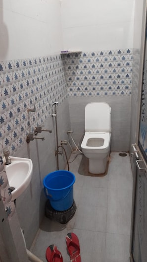 A small bathroom with a toilet, sink, and blue bucket. - Maruti Nandan Hotel (Rajnagar)