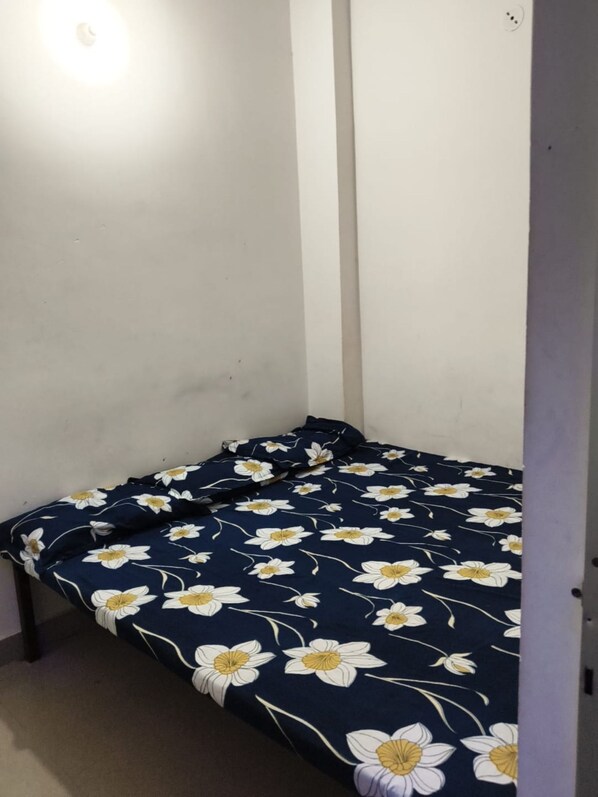 A small, single-bed room with a floral-patterned bedspread. - Maruti Nandan Hotel (Rajnagar)