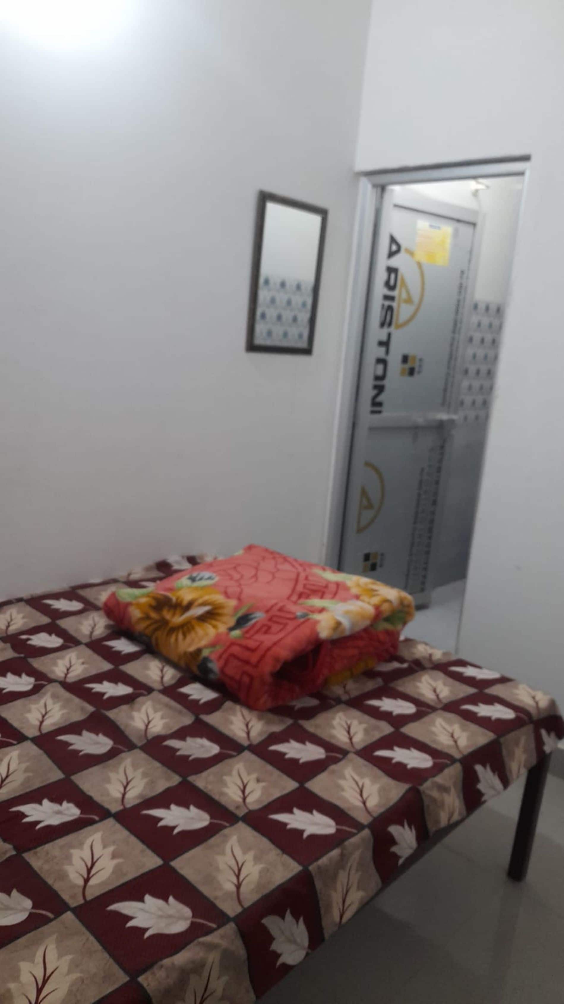 Una habitación con una cama cubierta por una colcha estampada, una puerta con cerradura y un pequeño cuadro enmarcado en la pared.