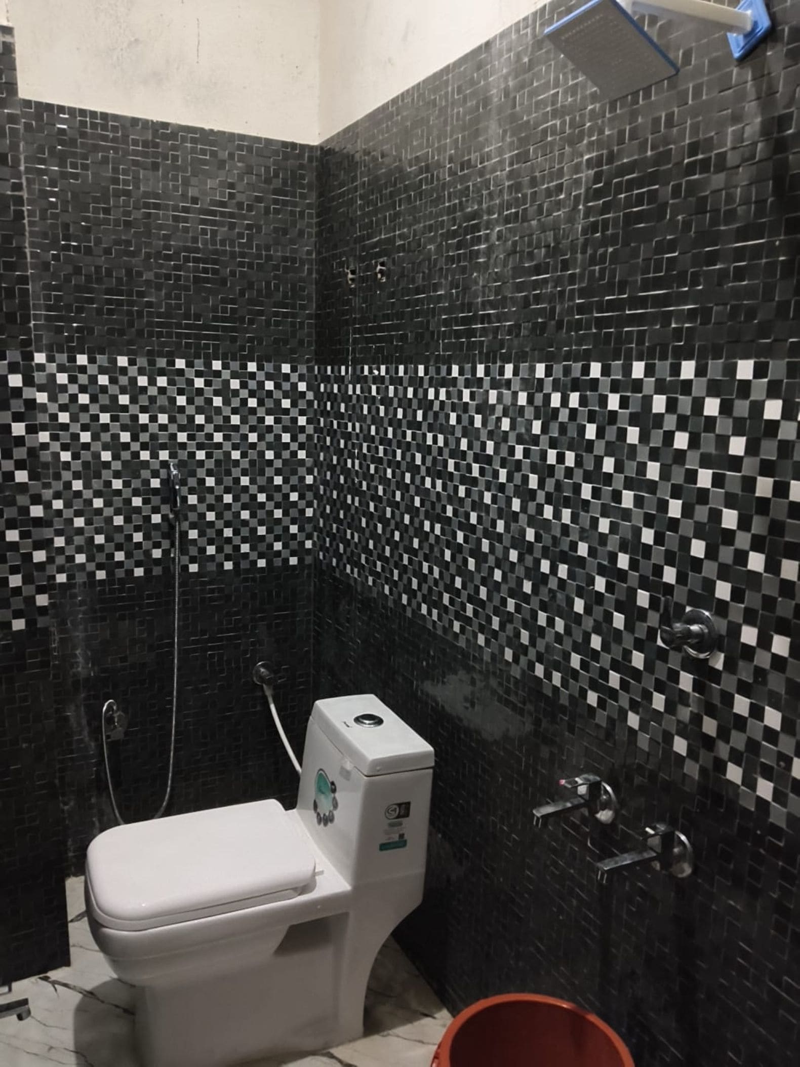 A bathroom with a toilet, a shower, and a tiled wall.
