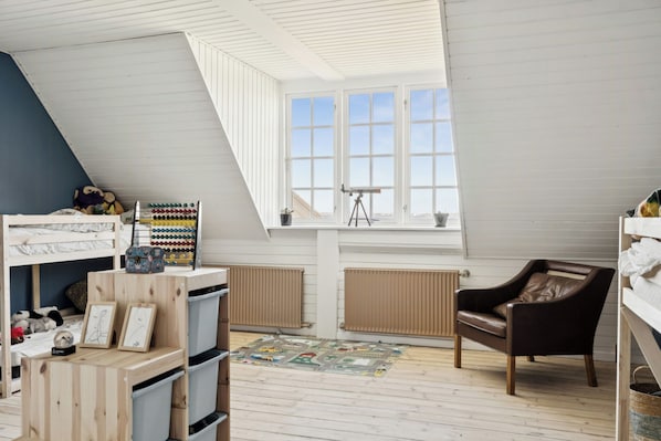 Een kamer met een schuine kap, een raam met veel ruitjes, een telescoop en een fauteuil van bruin leer.