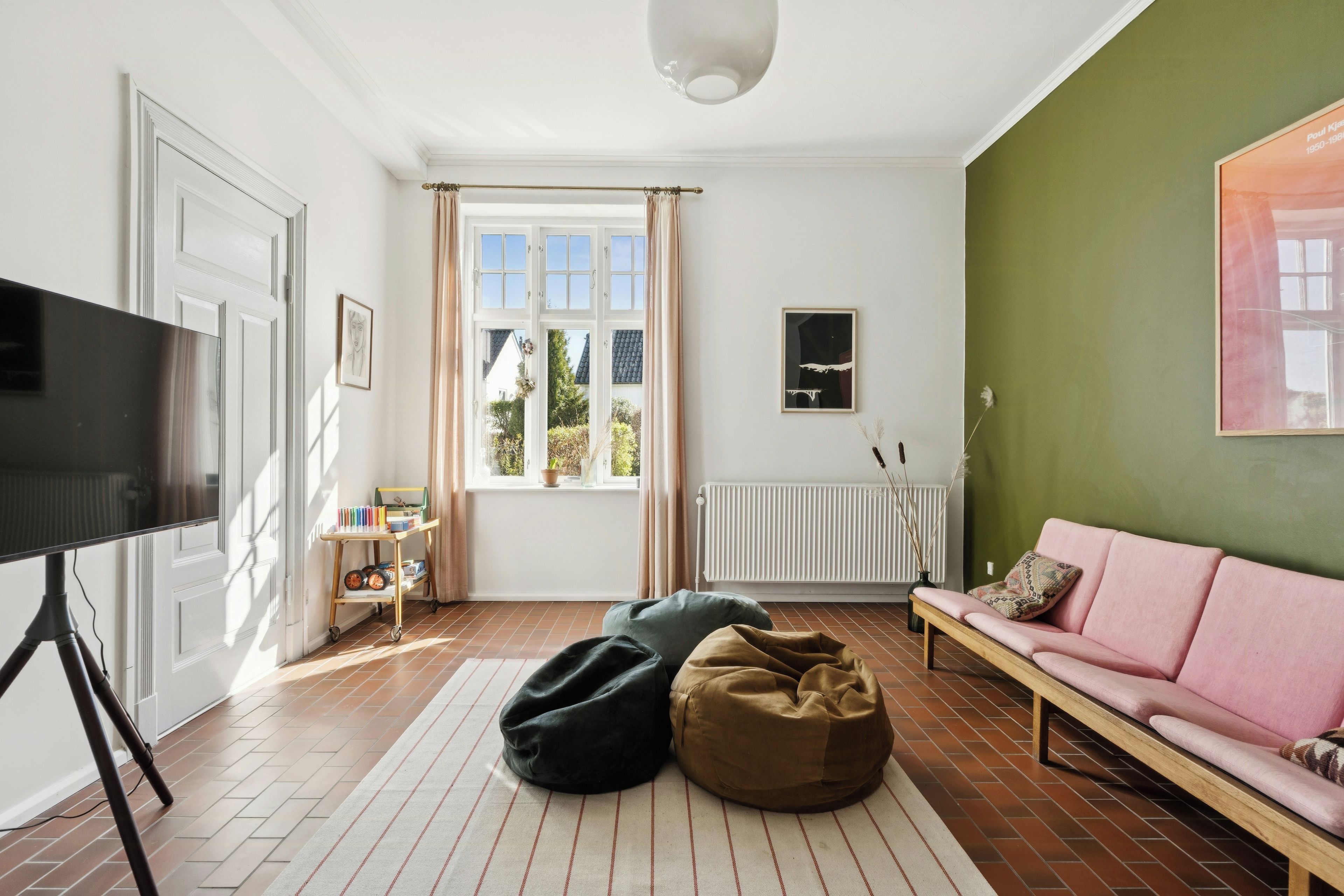 A living room with a television, a sofa, bean bags, a radiator, and a window with curtains.