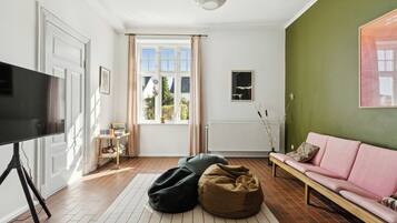 A living room with a television, a sofa, bean bags, a radiator, and a window with curtains.