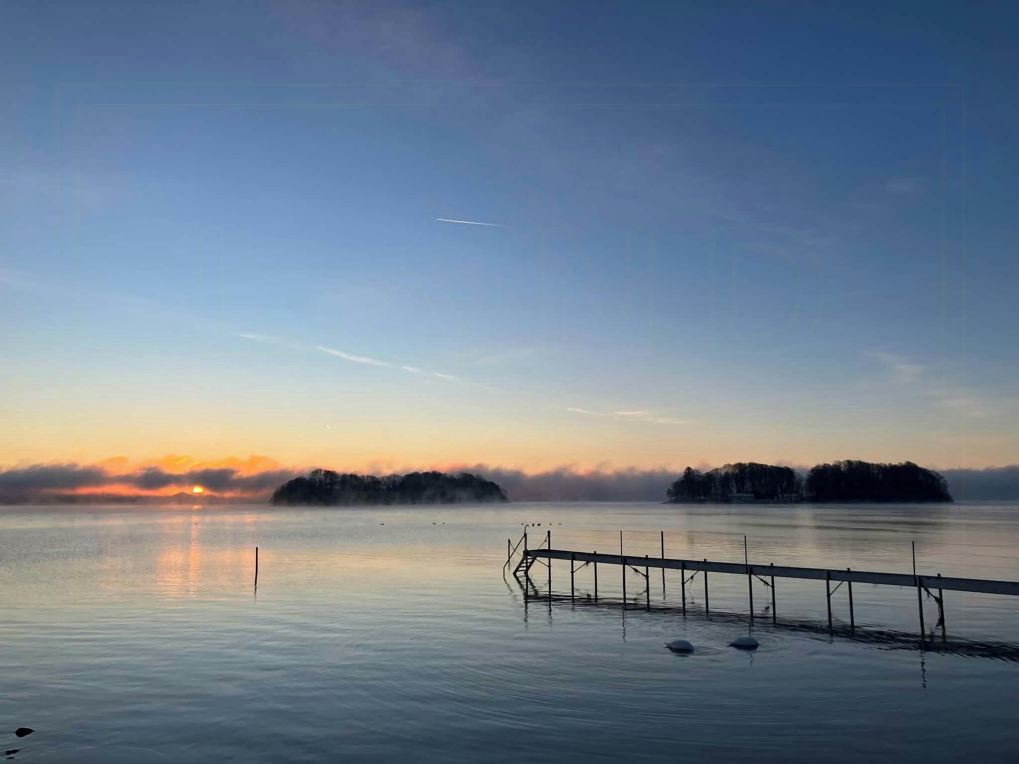 Un lac paisible, avec une jetée en bois qui s’avance sur l’eau, entouré d’îles enveloppées de brume.