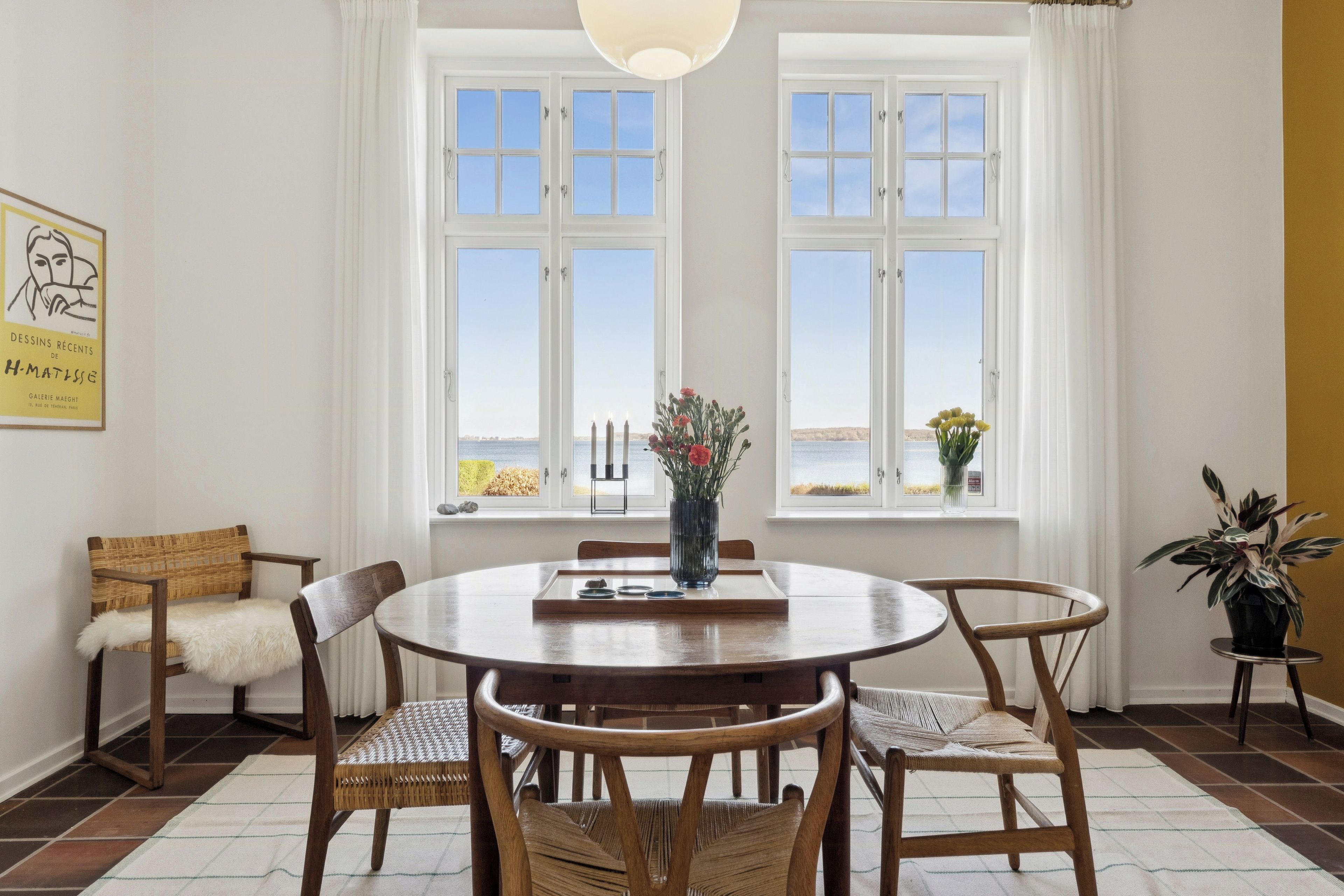 A dining area with a round table, chairs, and a view of the sea through large windows.