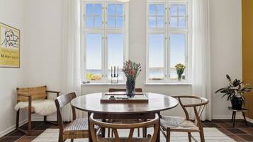 A dining area with a round table, chairs, and a view of the sea through large windows.